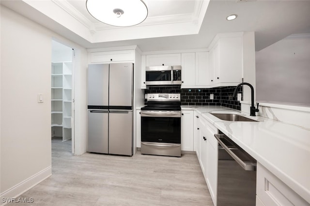 kitchen with appliances with stainless steel finishes, a tray ceiling, a sink, and ornamental molding