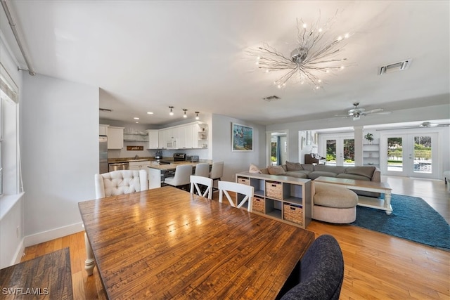 dining area with ceiling fan with notable chandelier, light hardwood / wood-style flooring, and french doors