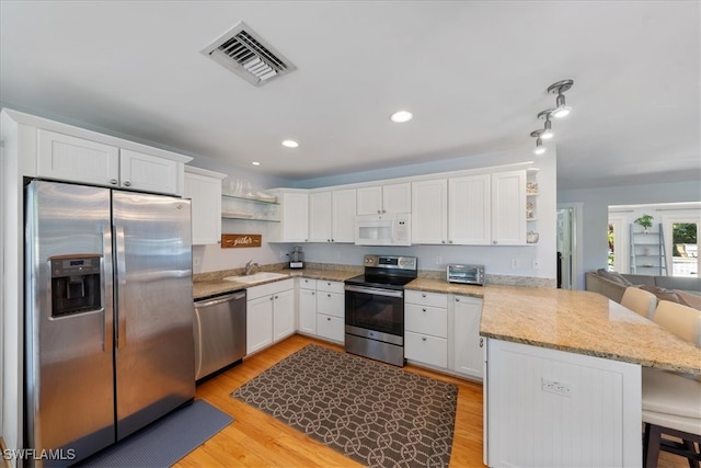 kitchen featuring appliances with stainless steel finishes, light hardwood / wood-style floors, white cabinets, kitchen peninsula, and a breakfast bar area