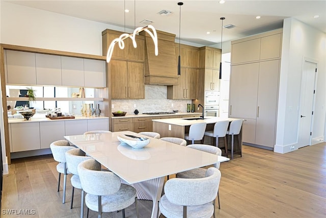 kitchen featuring backsplash, stainless steel gas cooktop, a center island with sink, light hardwood / wood-style flooring, and hanging light fixtures