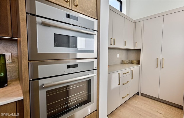 kitchen with decorative backsplash, light wood-type flooring, white cabinetry, and double oven