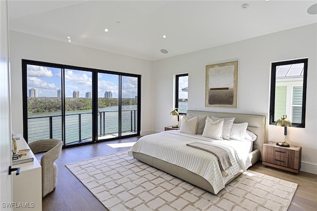 bedroom with access to outside, a water view, and hardwood / wood-style flooring