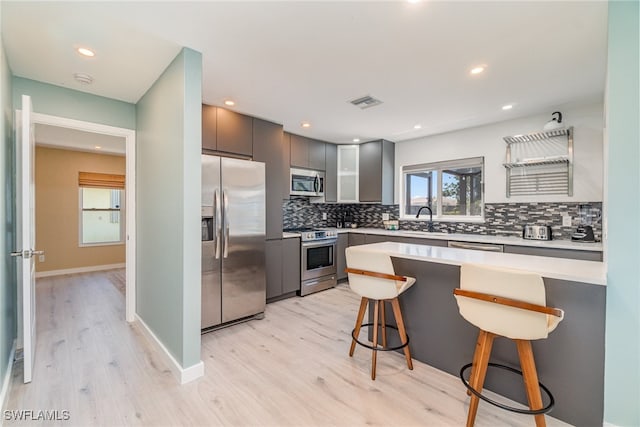 kitchen with gray cabinetry, sink, light wood-type flooring, a kitchen bar, and stainless steel appliances