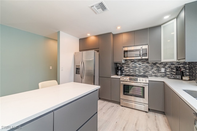 kitchen featuring gray cabinets, light hardwood / wood-style floors, appliances with stainless steel finishes, and tasteful backsplash