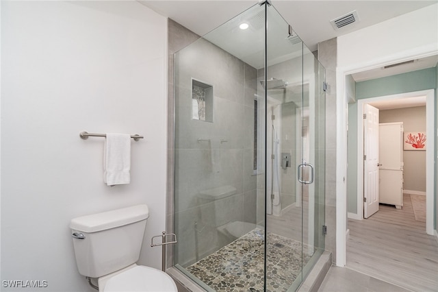 bathroom with hardwood / wood-style floors, toilet, and a shower with door