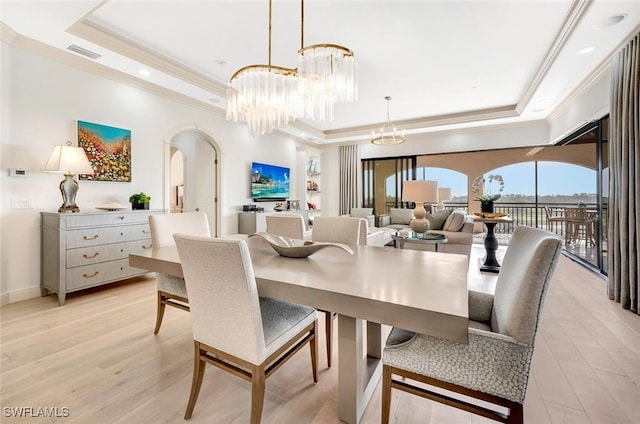 dining area with crown molding, a notable chandelier, light wood-type flooring, and a raised ceiling