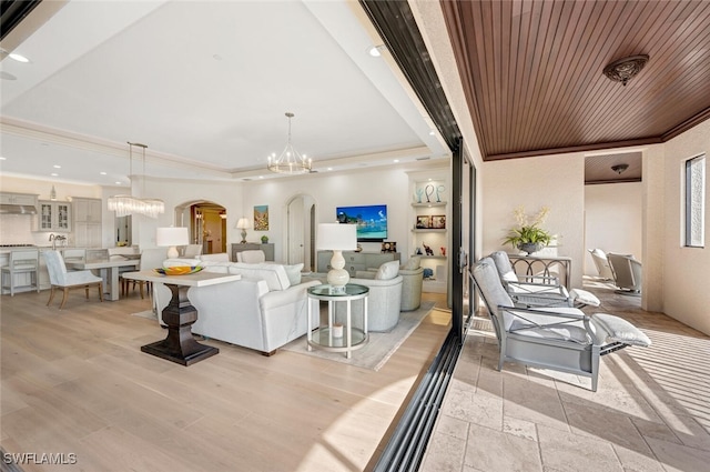 living room with light wood-type flooring, a raised ceiling, wooden ceiling, a notable chandelier, and ornamental molding