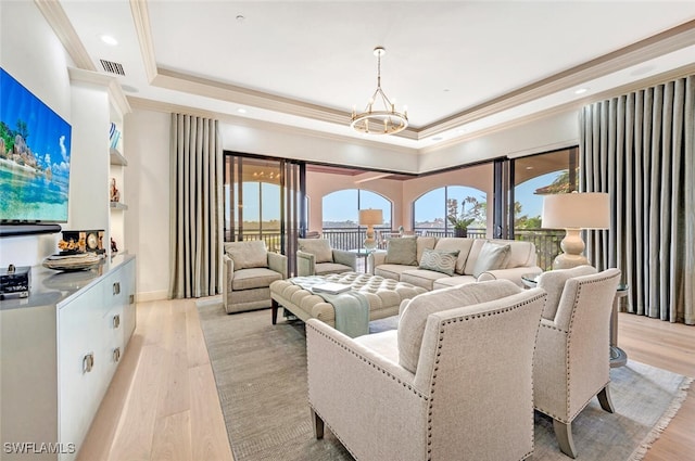 living room with ornamental molding, light hardwood / wood-style flooring, an inviting chandelier, and a raised ceiling