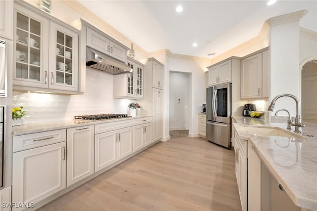 kitchen featuring decorative backsplash, light stone counters, appliances with stainless steel finishes, light hardwood / wood-style floors, and sink