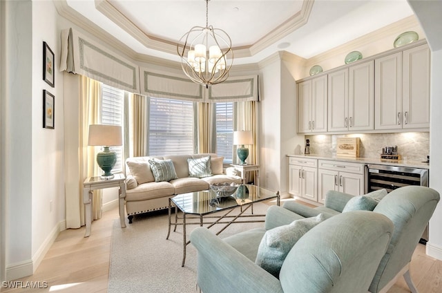 living room with wine cooler, a chandelier, a tray ceiling, ornamental molding, and light hardwood / wood-style floors