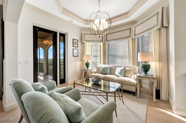 living room with light hardwood / wood-style floors, crown molding, a tray ceiling, and a chandelier