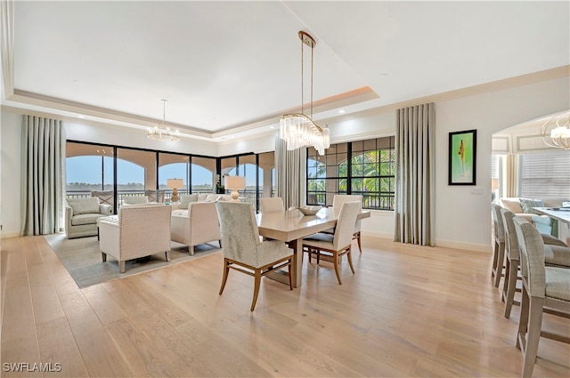 dining area with a notable chandelier, light hardwood / wood-style flooring, and a raised ceiling