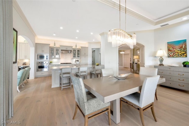 dining area with ornamental molding, sink, and light wood-type flooring