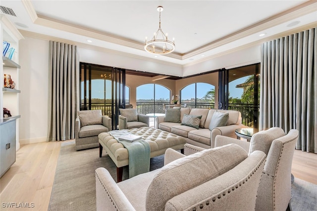 living room featuring ornamental molding, light hardwood / wood-style flooring, a notable chandelier, and a raised ceiling