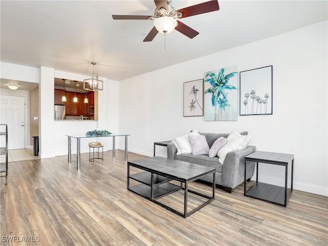 living room featuring ceiling fan with notable chandelier and light hardwood / wood-style flooring