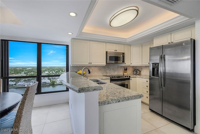 kitchen with a tray ceiling, light tile patterned floors, appliances with stainless steel finishes, a sink, and a peninsula