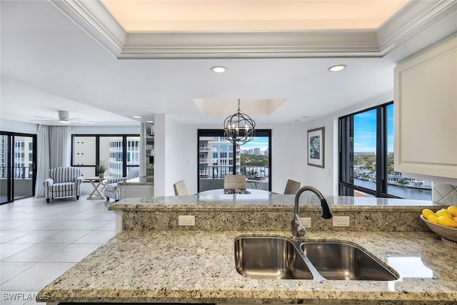 kitchen with light tile patterned floors, light stone counters, a tray ceiling, a sink, and recessed lighting