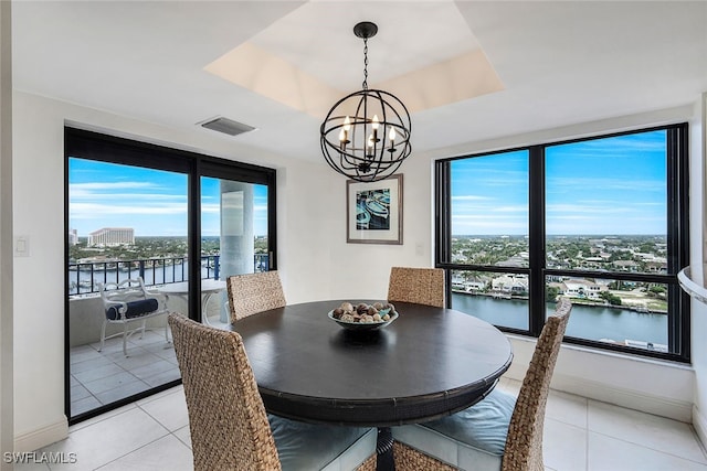 dining area with a tray ceiling, a water view, visible vents, and light tile patterned floors