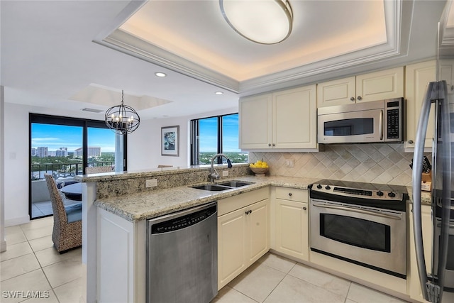 kitchen featuring stainless steel appliances, a raised ceiling, decorative backsplash, a sink, and a peninsula