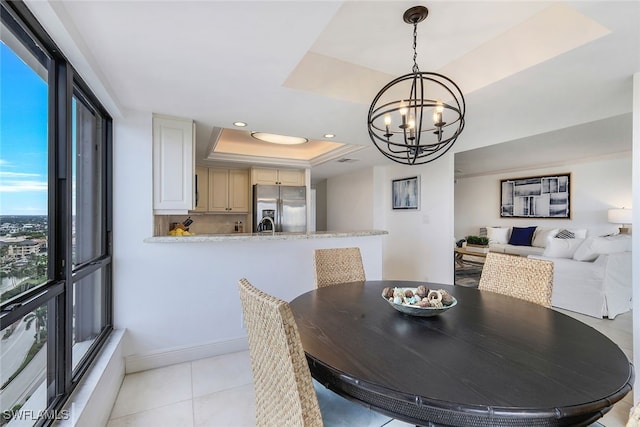 dining area featuring light tile patterned floors, a tray ceiling, an inviting chandelier, and a healthy amount of sunlight