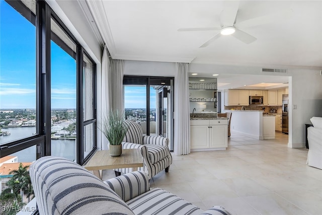 living area with ornamental molding, visible vents, a water view, and ceiling fan