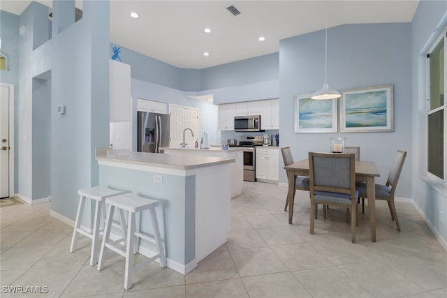 kitchen featuring decorative light fixtures, light tile patterned floors, appliances with stainless steel finishes, kitchen peninsula, and white cabinets