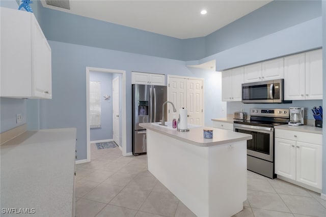 kitchen with white cabinets, light tile patterned floors, stainless steel appliances, and a kitchen island with sink