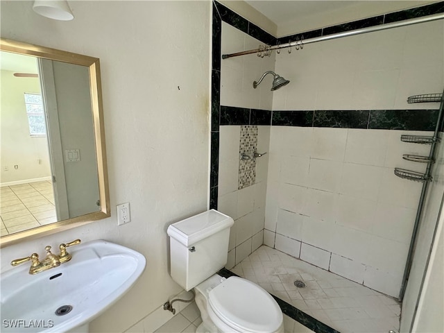 bathroom featuring tiled shower, toilet, sink, and tile patterned flooring