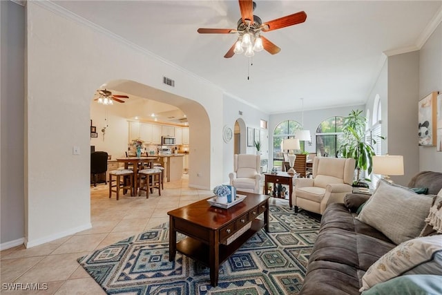 living room featuring arched walkways, light tile patterned floors, visible vents, baseboards, and crown molding