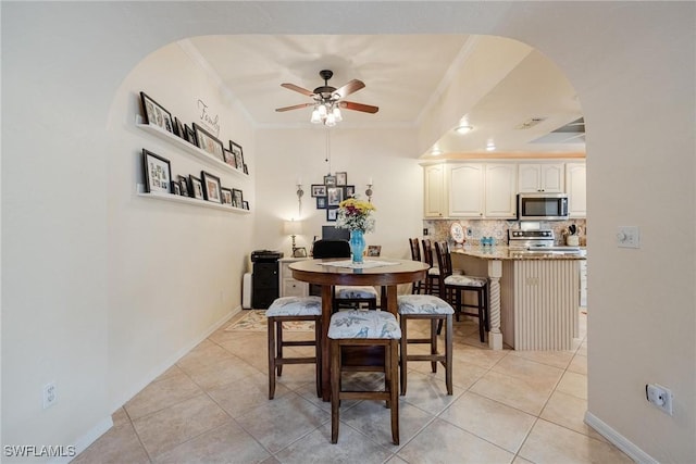 dining space with ceiling fan, light tile patterned floors, arched walkways, baseboards, and ornamental molding