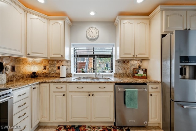 kitchen featuring stone countertops, backsplash, appliances with stainless steel finishes, sink, and cream cabinetry