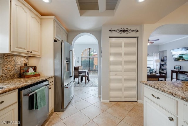 kitchen with light tile patterned floors, appliances with stainless steel finishes, arched walkways, and backsplash