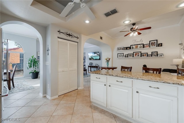 kitchen featuring light stone countertops, light tile patterned floors, ornamental molding, white cabinetry, and ceiling fan