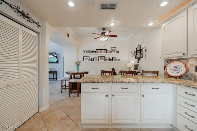 kitchen with crown molding, backsplash, light stone counters, ceiling fan, and white cabinets