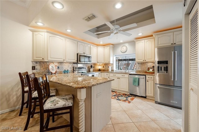 kitchen featuring stainless steel appliances, a peninsula, light stone countertops, tasteful backsplash, and a raised ceiling