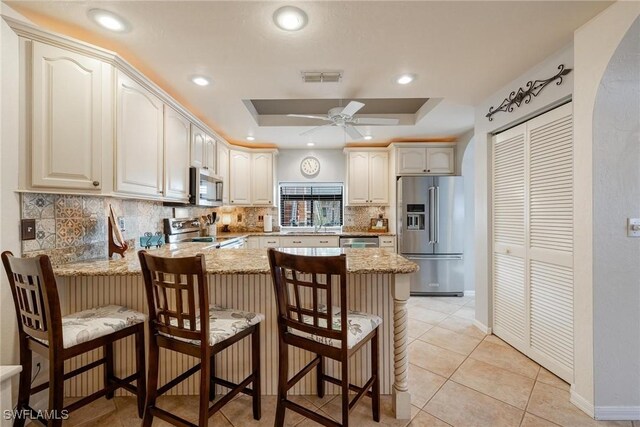 kitchen with a kitchen breakfast bar, stainless steel appliances, a raised ceiling, and kitchen peninsula