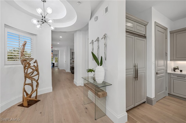 hallway featuring an inviting chandelier, a raised ceiling, and light hardwood / wood-style flooring