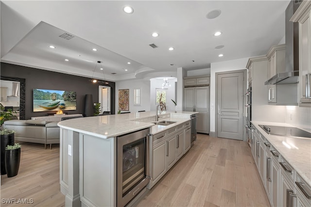 kitchen with wine cooler, decorative light fixtures, a center island with sink, light hardwood / wood-style floors, and wall chimney range hood