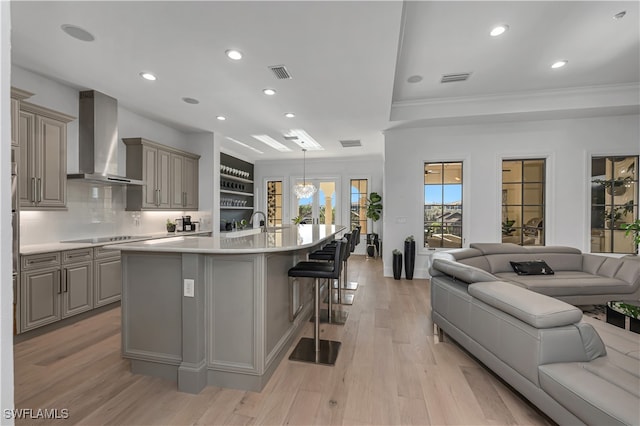 kitchen featuring a kitchen breakfast bar, pendant lighting, light hardwood / wood-style floors, a kitchen island with sink, and wall chimney range hood