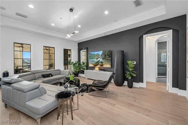 living room featuring a raised ceiling, ornamental molding, and light hardwood / wood-style floors