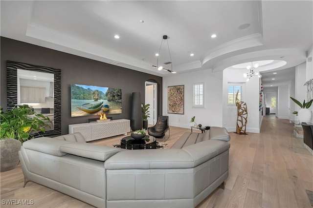 living room with light wood-type flooring, an inviting chandelier, and a tray ceiling