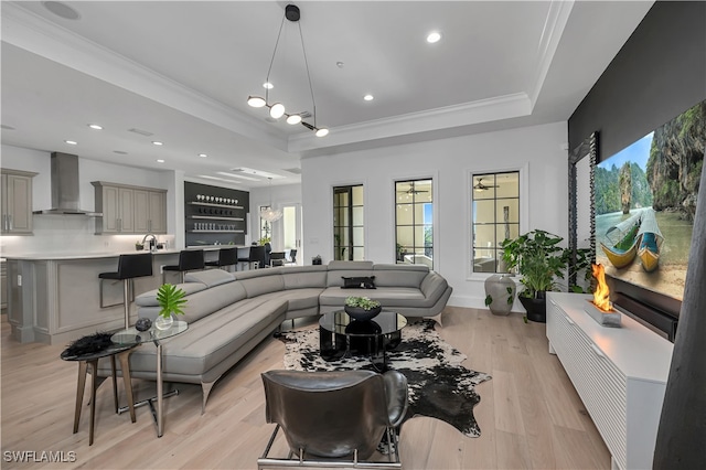 living room with light wood-type flooring, a raised ceiling, and crown molding