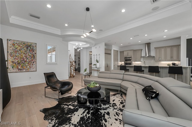 living room featuring light wood-type flooring, a raised ceiling, crown molding, and a notable chandelier