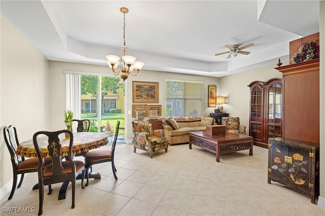 tiled living room featuring ceiling fan with notable chandelier and a tray ceiling