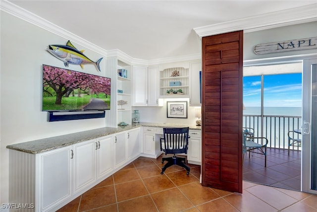 home office with dark tile patterned flooring, built in study area, crown molding, and a water view