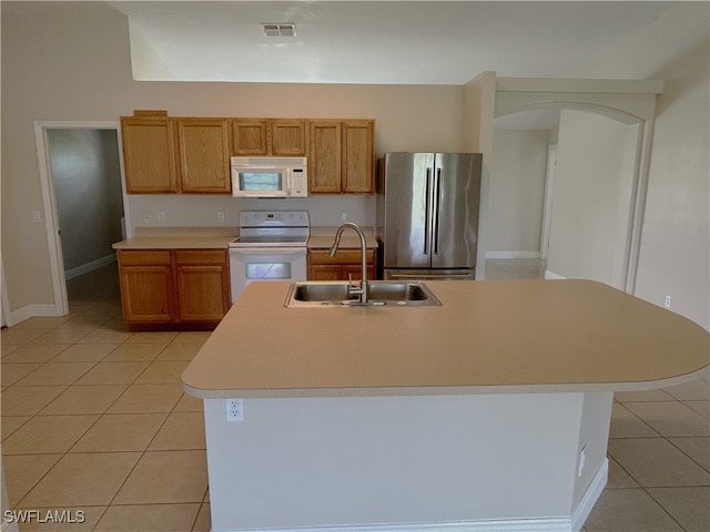 kitchen featuring light tile patterned flooring, an island with sink, sink, and white appliances