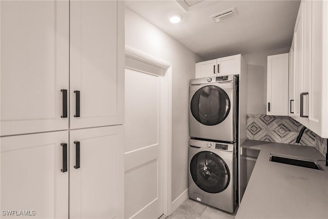 laundry room featuring cabinet space, visible vents, stacked washer / drying machine, a sink, and light tile patterned flooring