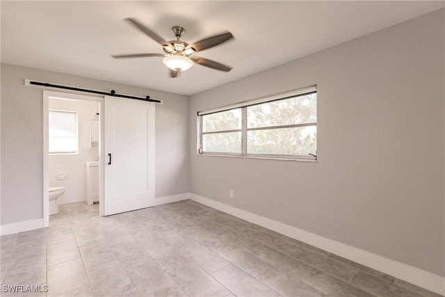 unfurnished bedroom with a barn door, baseboards, ceiling fan, and connected bathroom