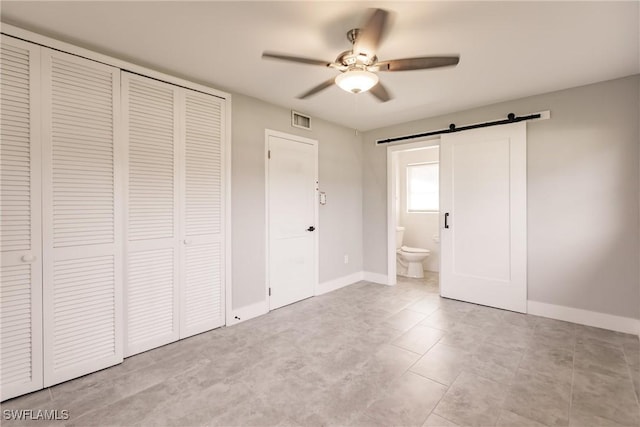 unfurnished bedroom featuring a closet, visible vents, baseboards, and a barn door