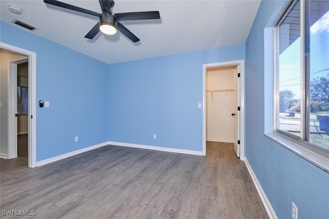 unfurnished bedroom with a walk in closet, ceiling fan, a closet, and wood-type flooring